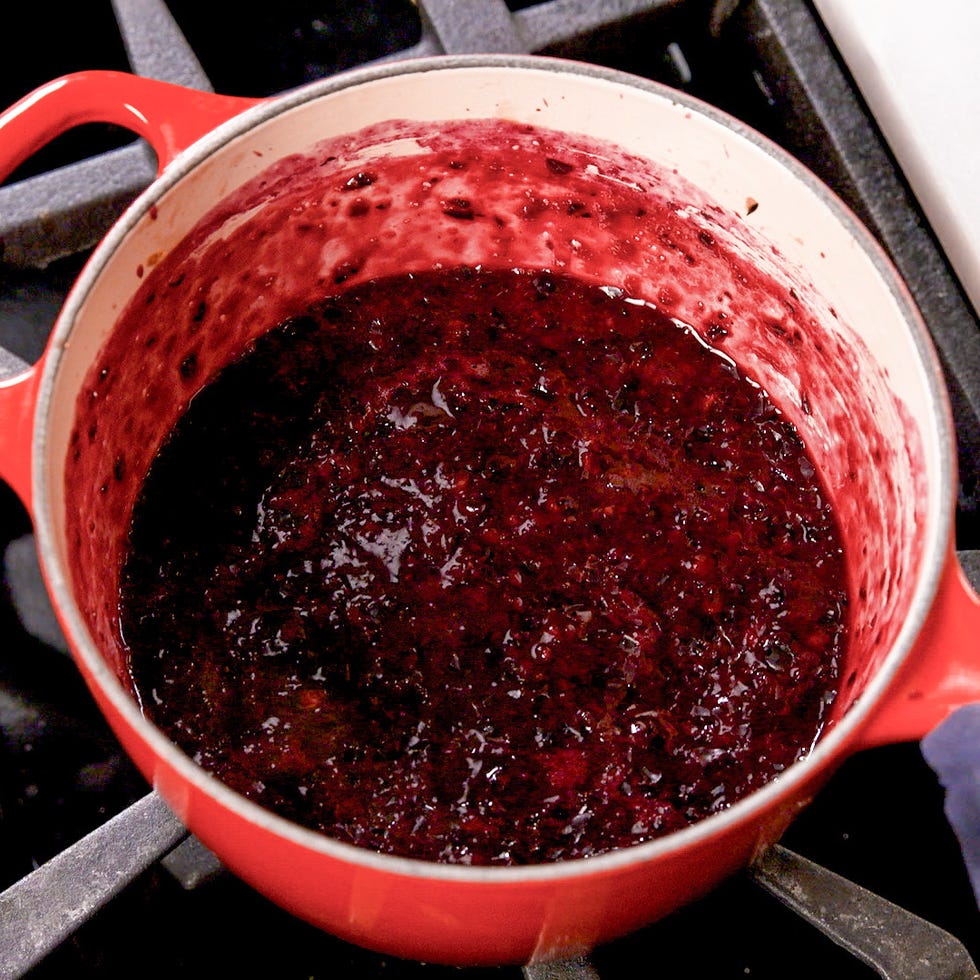 cooking blueberry puree in a red pot on a stove.