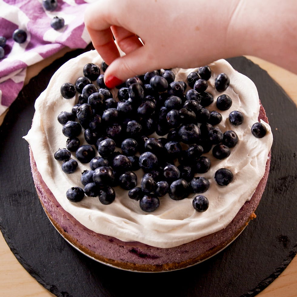 blueberry topping being added to a cream covered cake