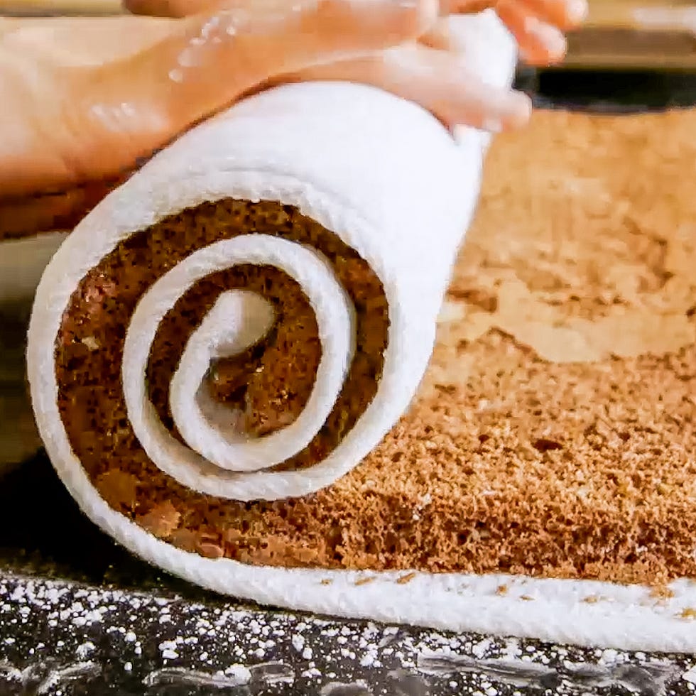 a hand rolling a chocolate cake with a white towel