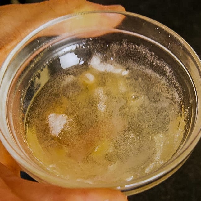 a hand holding a clear glass containing a frothy yellowish liquid