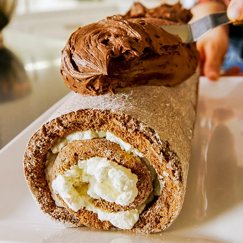 chocolate roll cake being prepared with whipped cream filling