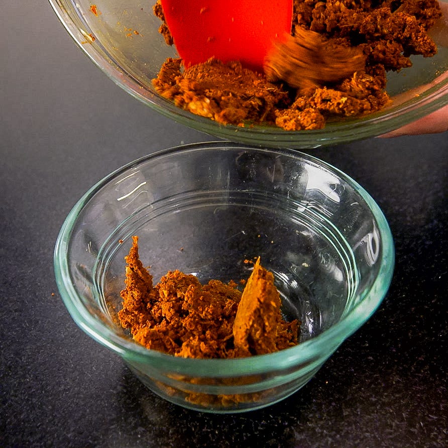transfer of a thick brown paste from a bowl to a smaller glass dish using a spatula