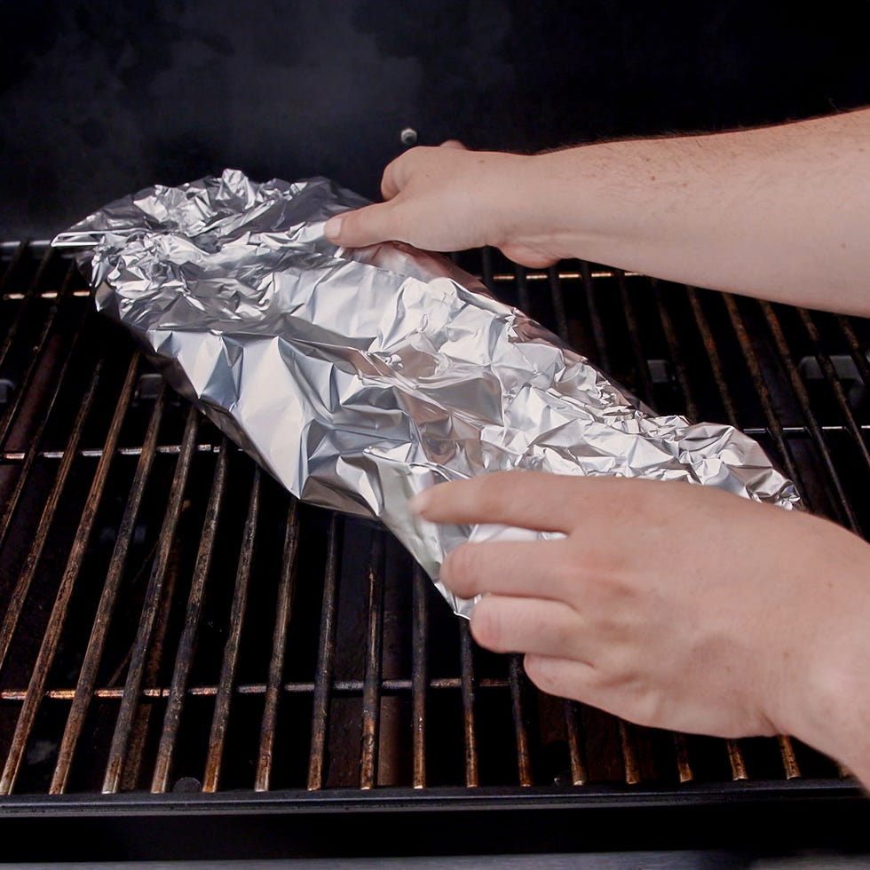 hands placing foil wrapped ribs on a grill