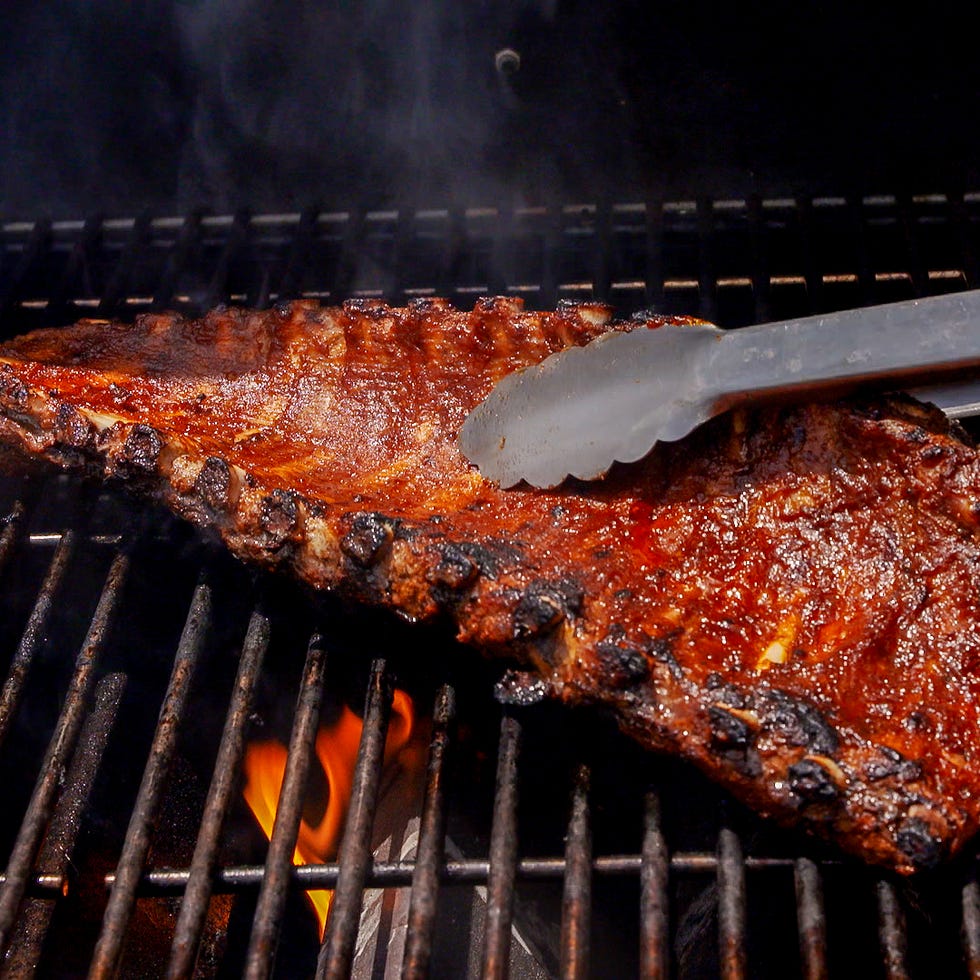 grilled ribs being turned on a barbecue grill
