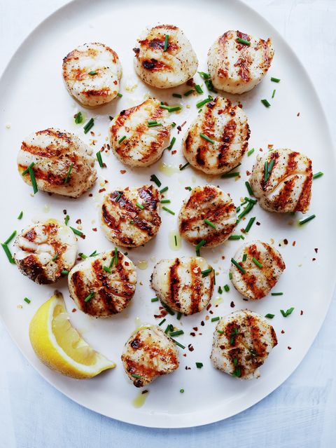 grilled scallops on a white plate garnished with lemon and chives