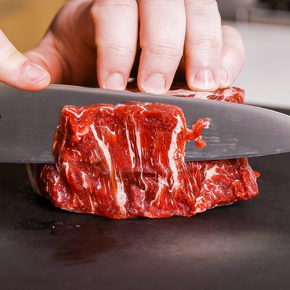 slicing raw beef with a chefs knife on a cutting board
