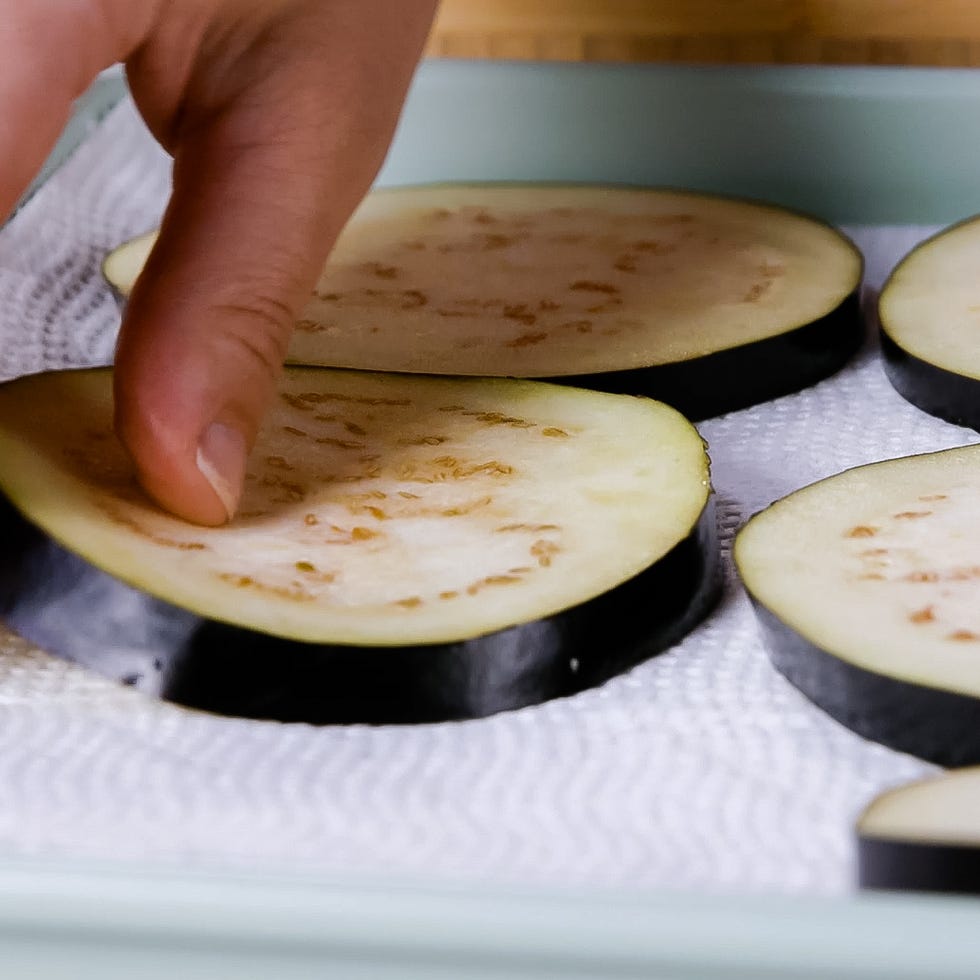 hand picking up sliced eggplant on a paper towel