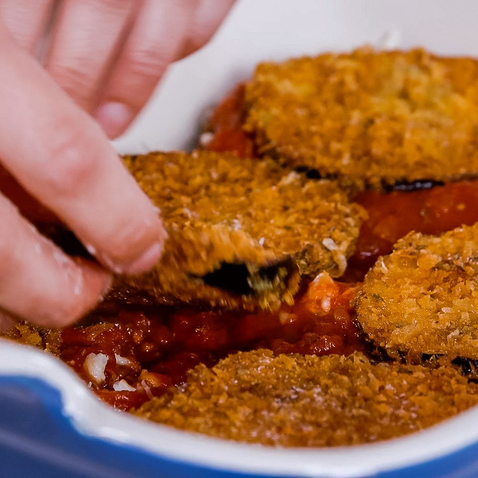 layering fried eggplant slices on top of a tomato sauce in a baking dish