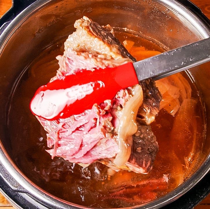 cooked meat being lifted from a pot with a spatula