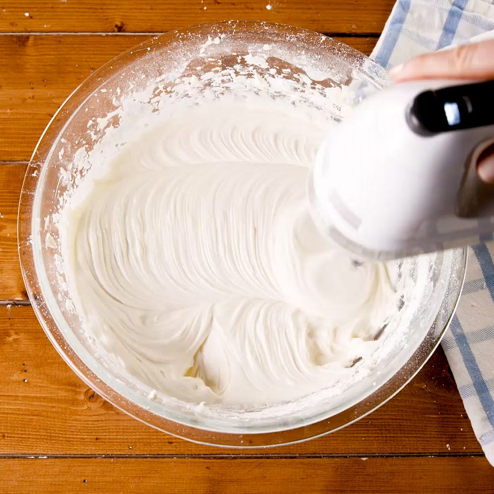 beating cream cheese frosting with a handheld mixer