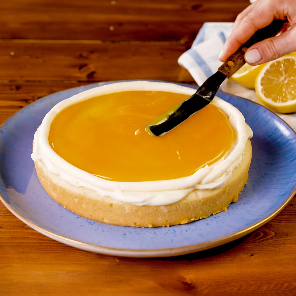 spreading lemon curd on frosting on a layer of cake