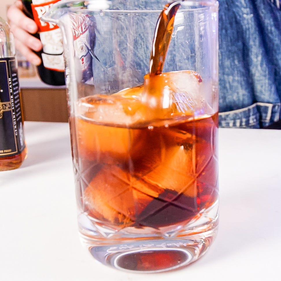a glass of a dark beverage with ice being poured from a bottle