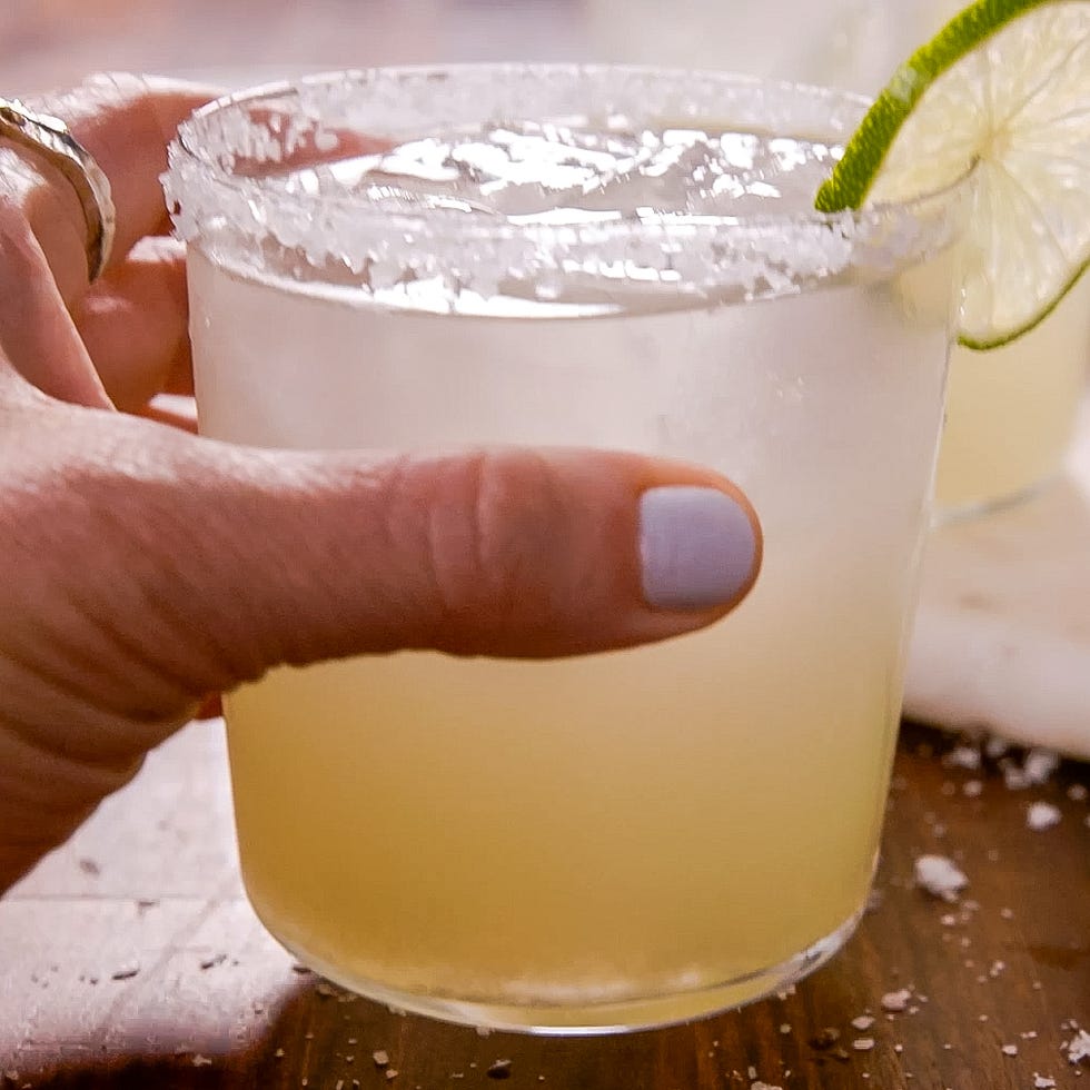 a hand holding a cocktail glass with salted rim and lime garnish