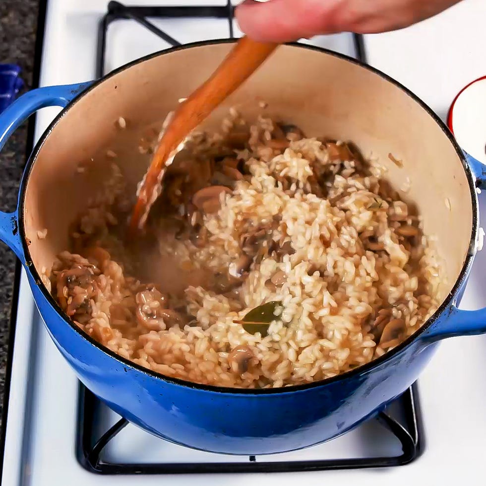 stirring risotto with mushrooms in a pot on a stovetop