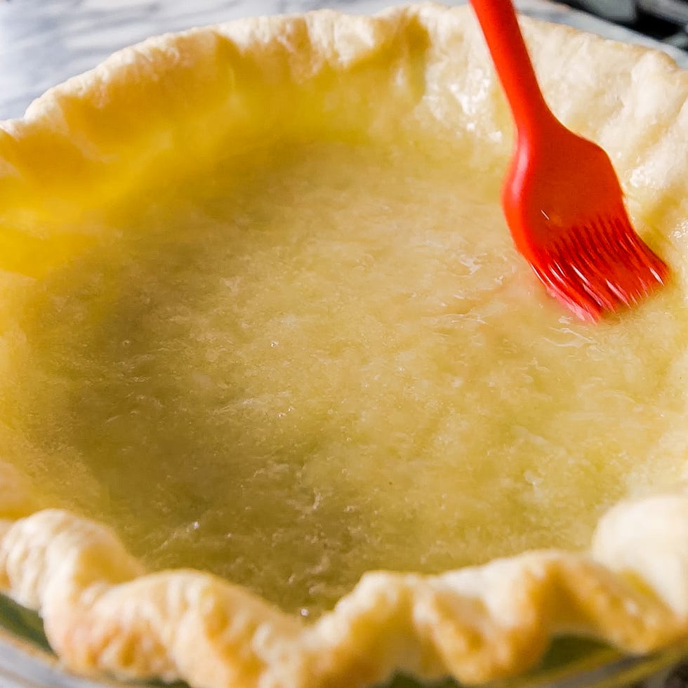 a pie crust with a yellow filling being brushed with a red utensil