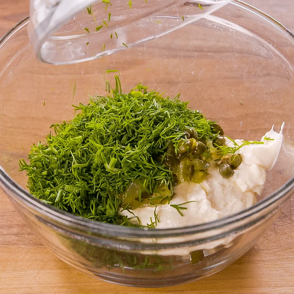 bowl containing a mixture of mayonnaise chopped herbs and green ingredients