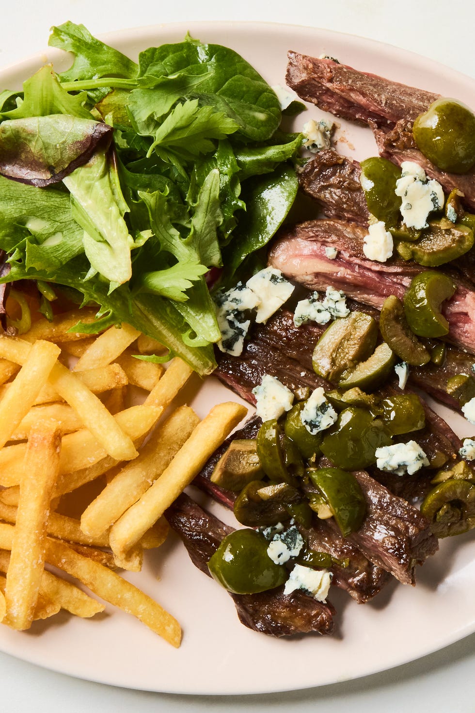 Dirty Martini Steak Frites seared skirt steak topped with buttery green olive, gin, and vermouth sauce and served with crispy golden french fries