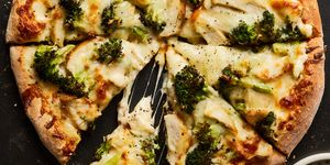 chicken broccoli alfredo pizza sliced into wedges on a black sheet pan