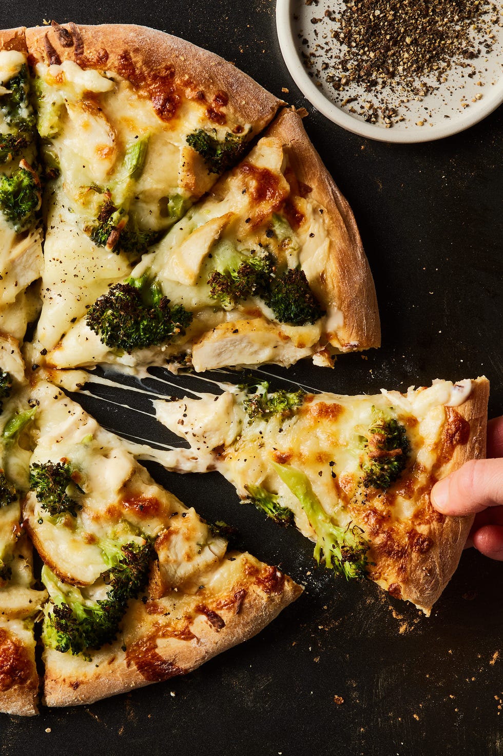chicken broccoli alfredo pizza cut into slices on a black baking sheet