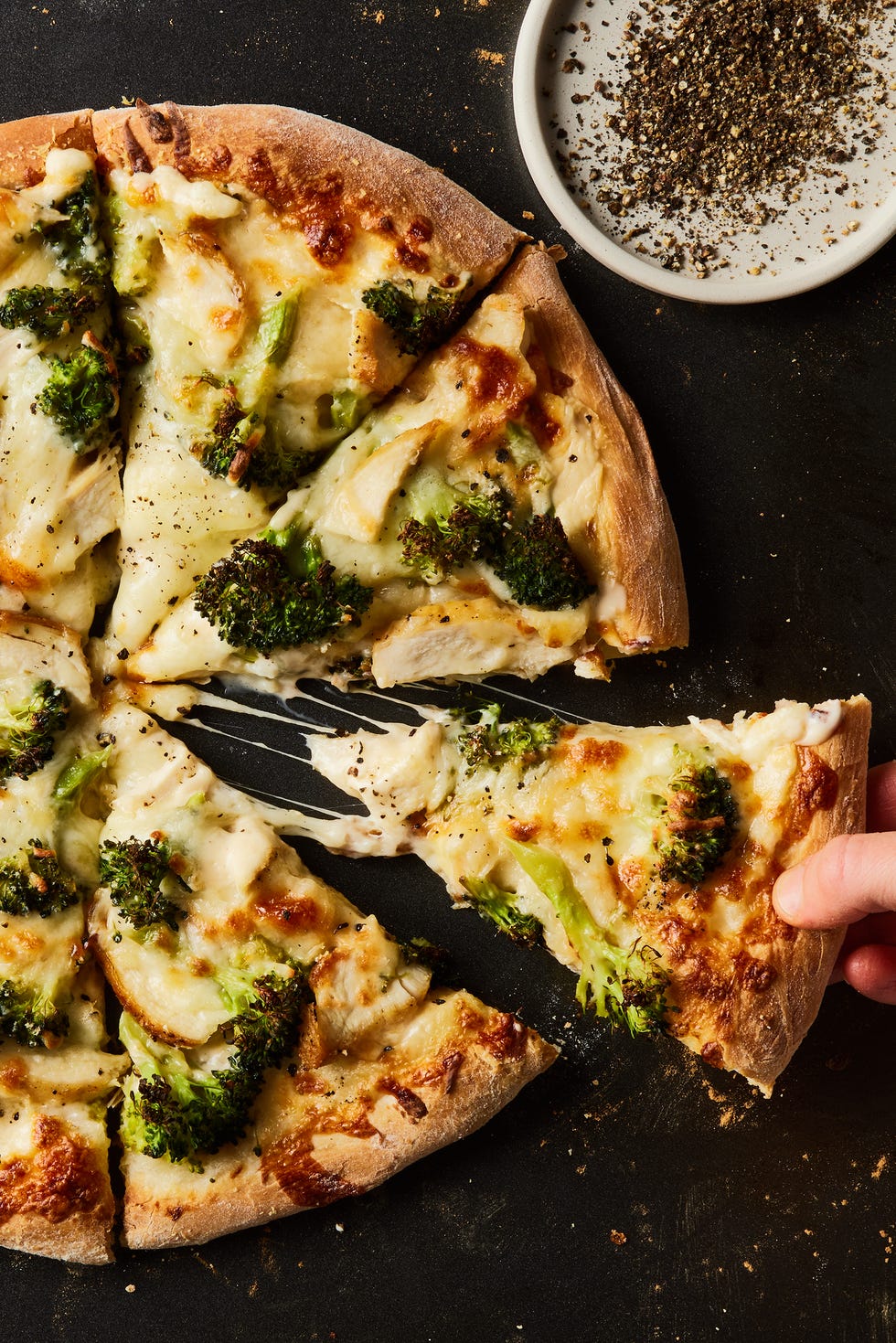 chicken broccoli alfredo pizza cut into slices on a black baking sheet