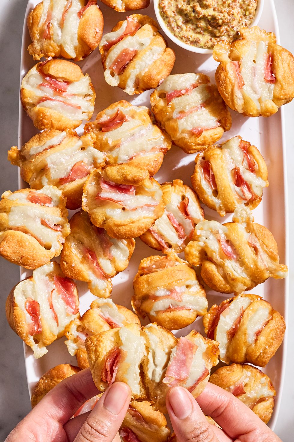 ham and swiss hasselback biscuit bites on a white tray with a bowl of dijon mustard