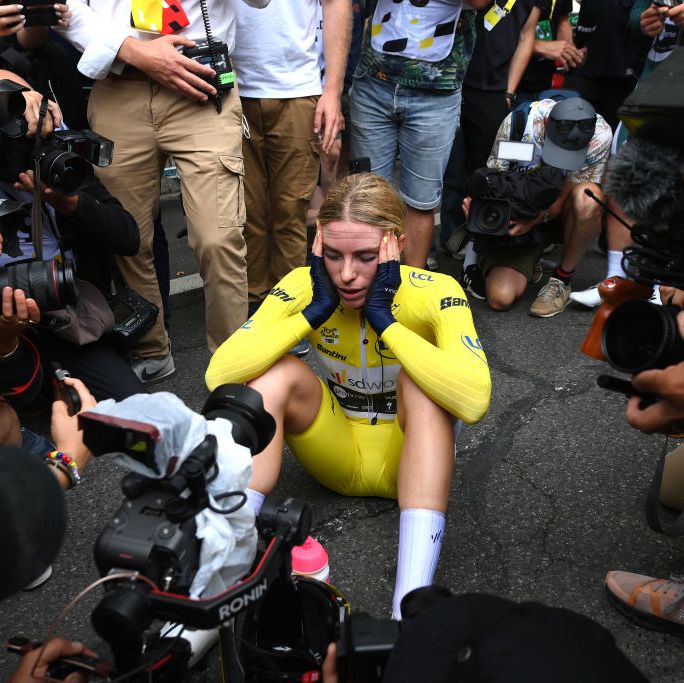 a cyclist in a yellow skinsuit is surrounded by photographers after a race