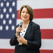 Sen.Amy Klobuchar senator amy klobuchar holding a microphone and standing in front of an american flag