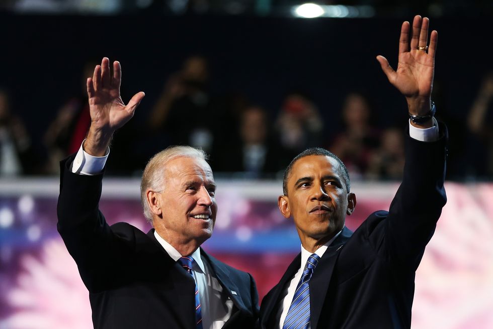 joe biden and barack obama stand in suits and wave