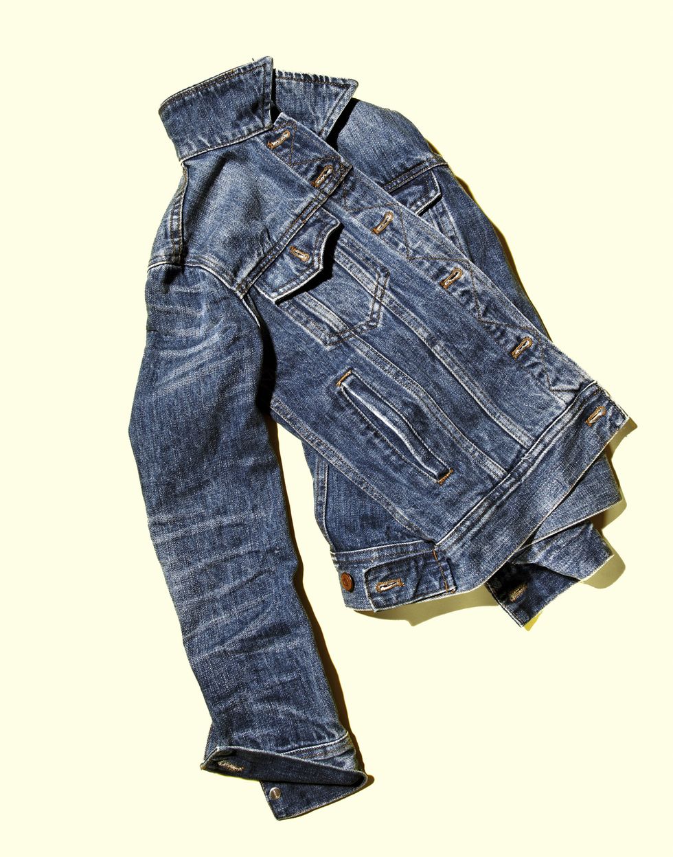 denim jacket laying artfully twisted on a white surface