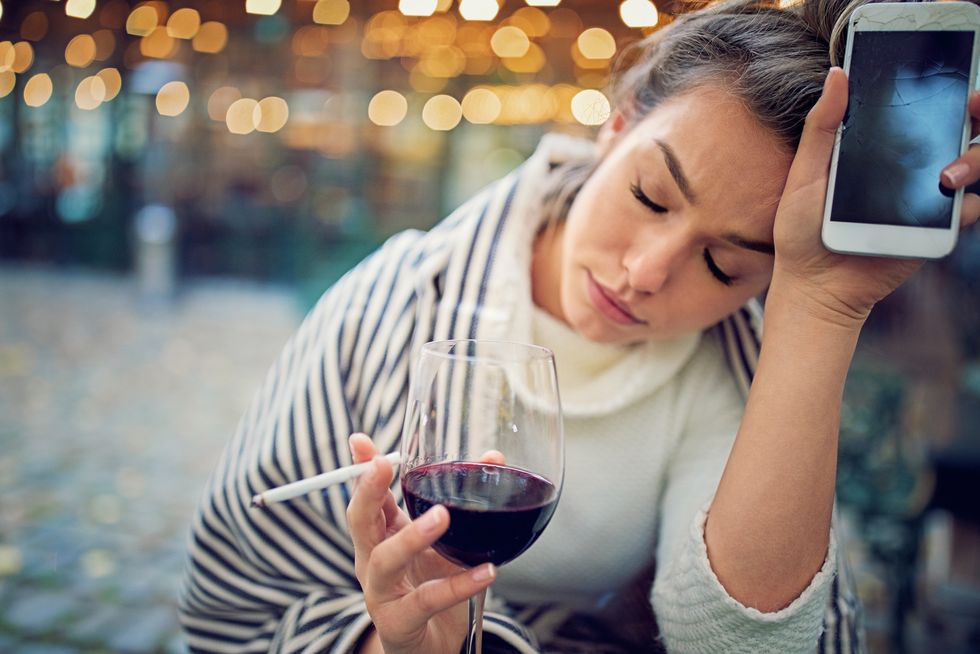 depressed woman is drinking wine and holding her broken phone in a rainy day