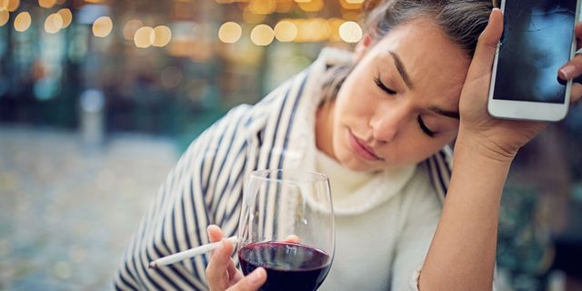Depressed woman is drinking wine and holding her broken phone in a rainy day