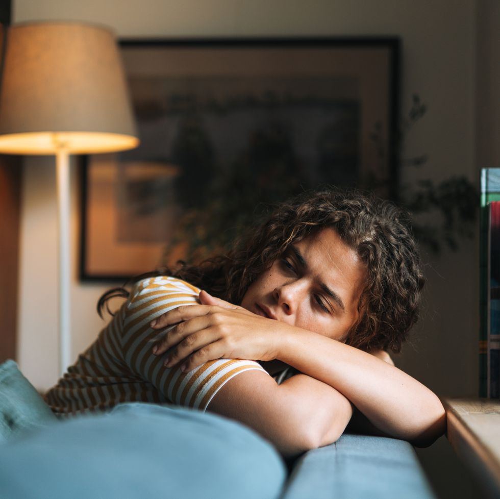 depressed woman with curly hair sitting on sofa in room at home