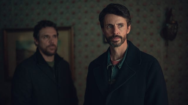 two individuals stand in a dimly lit room with vintage decor