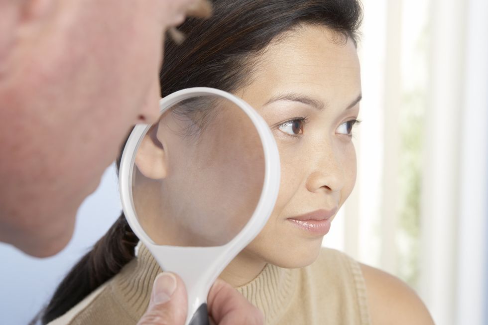 Dermatologist using magnifying glass to examine woman's skin