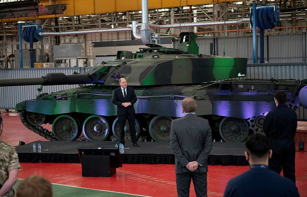 a person standing on a stage in front of a military tank