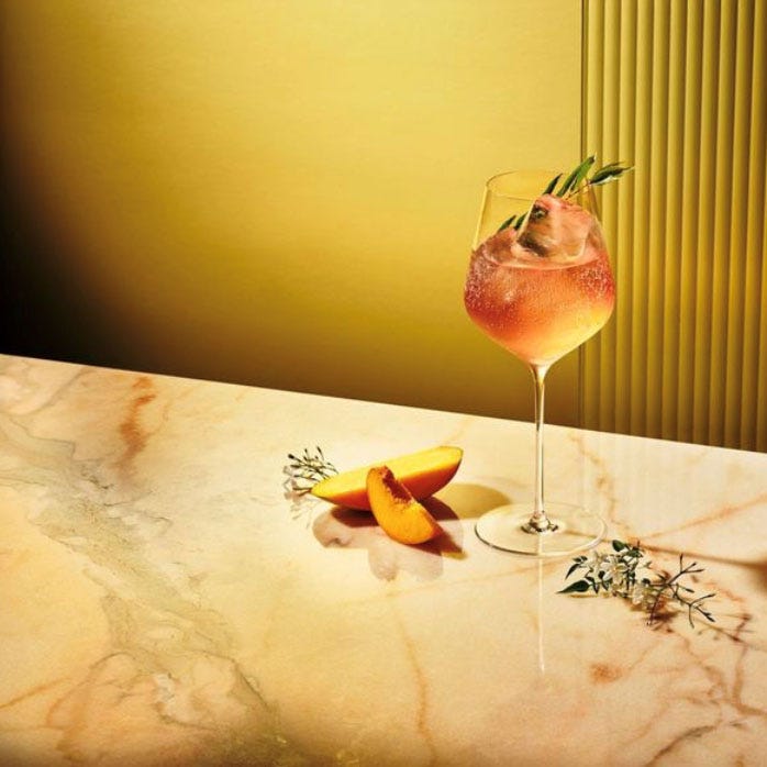 desi daru cocktail and peach slices on a marble surface