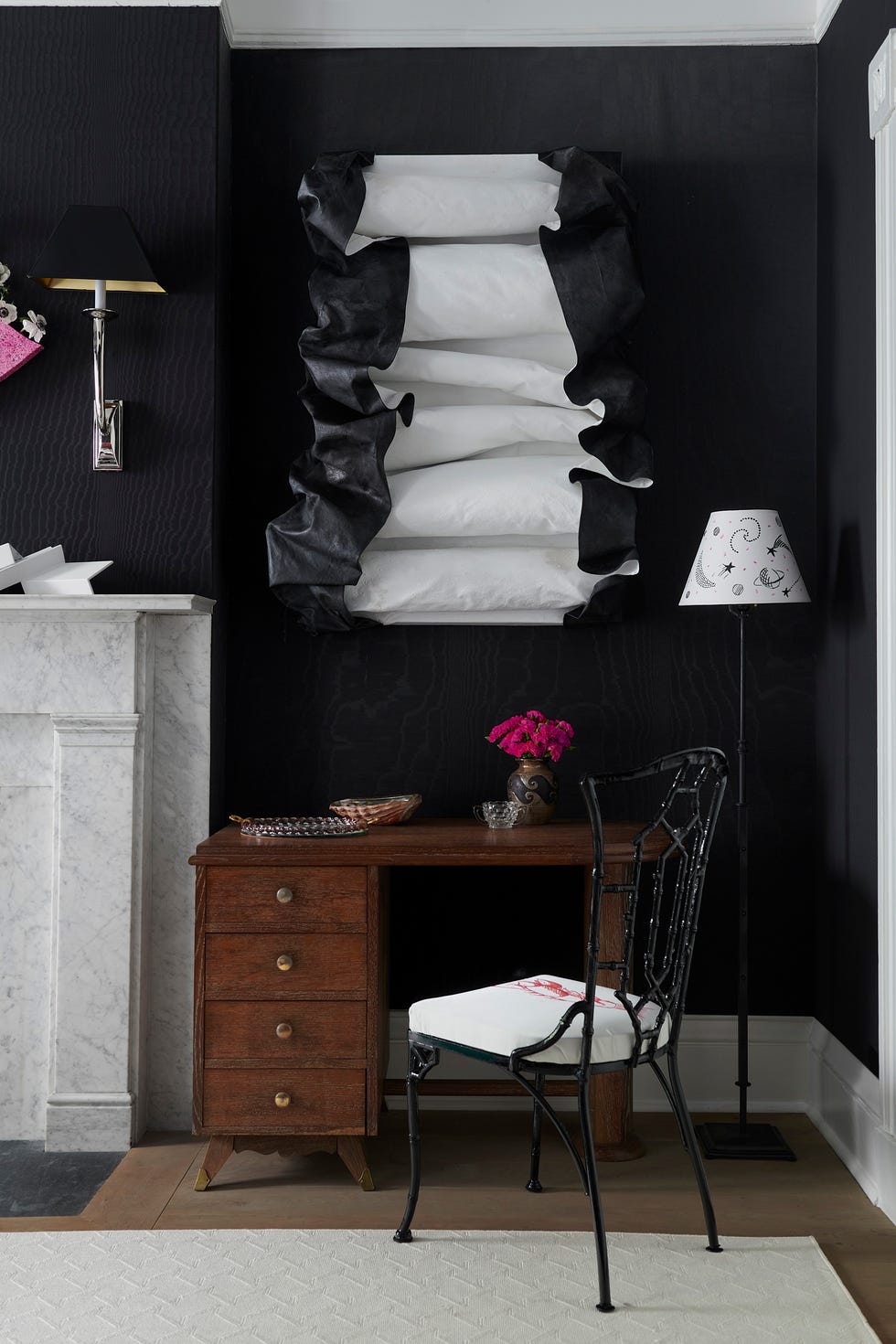 a black and white photo of a bedroom with a black chair and a desk with a lamp and