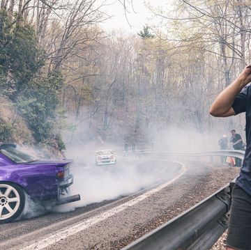 a man taking a picture of a car on a road with smoke coming out of it