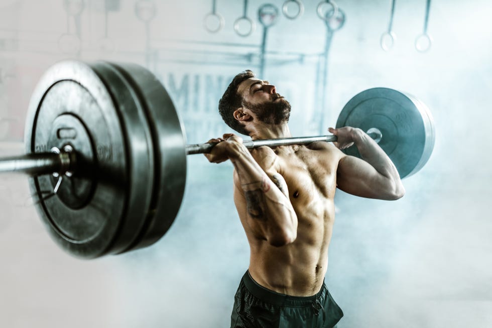 determined athletic man lifting heavy barbell in gym