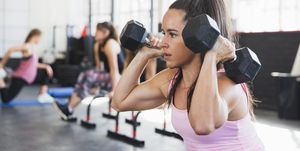 Determined, muscular young woman doing squats with dumbbells in gym