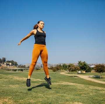 determined young women jumping while exercising at park against sky