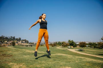 determined young women jumping while exercising at park against sky