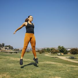 determined young women jumping while exercising at park against sky