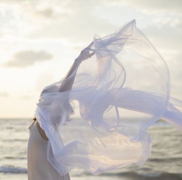 woman holding sheer fabric on a beach in the early morning light