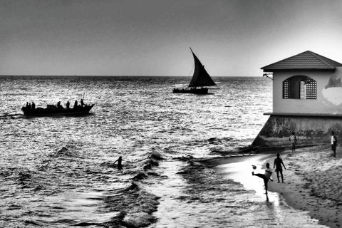 Vaargasten zeilers zwemmers en voetballers genieten van een zonnig dagje op het strand bij Stone Town op Zanzibar De stad was ooit een beruchte haven voor de OostAfrikaanse slavenhandel maar geldt nu als de multiculturele stad waar de Britse slavenhandel in 1873 officieel werd afgeschaft