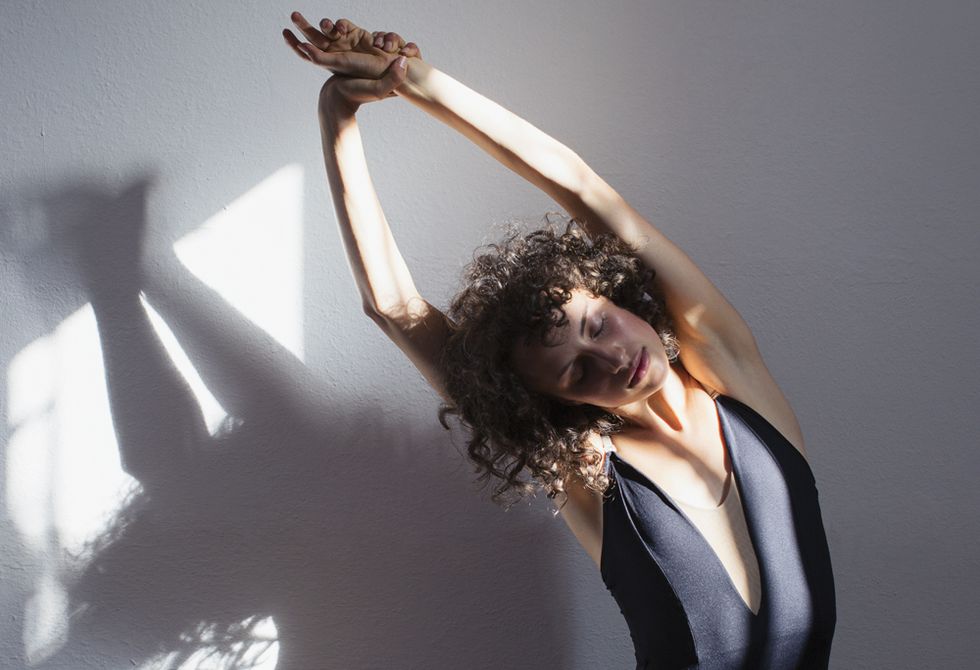 Sensual young female dancer stretching in sunlight at wall