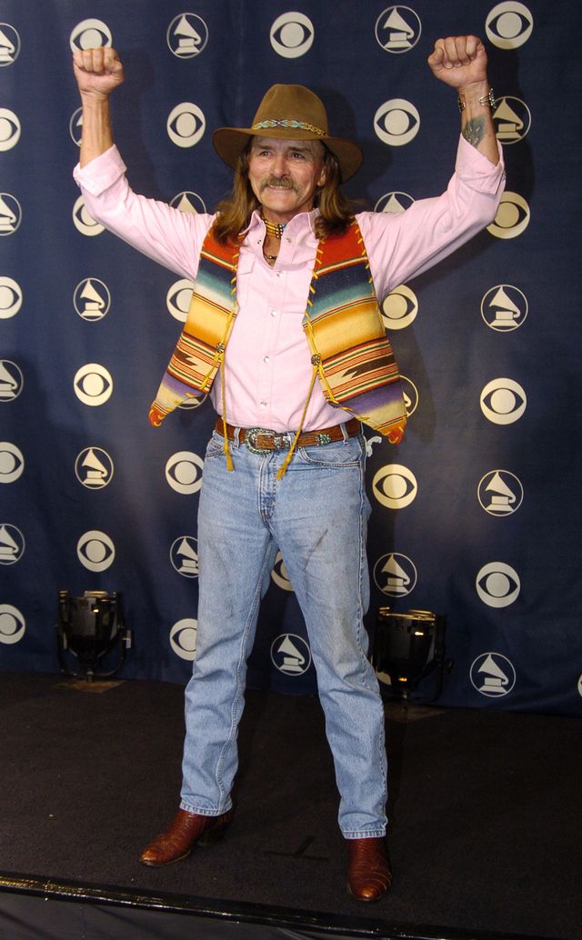 dickey betts wearing jeans and cowboy attire and raising his arms and fists in a celebratory pose
