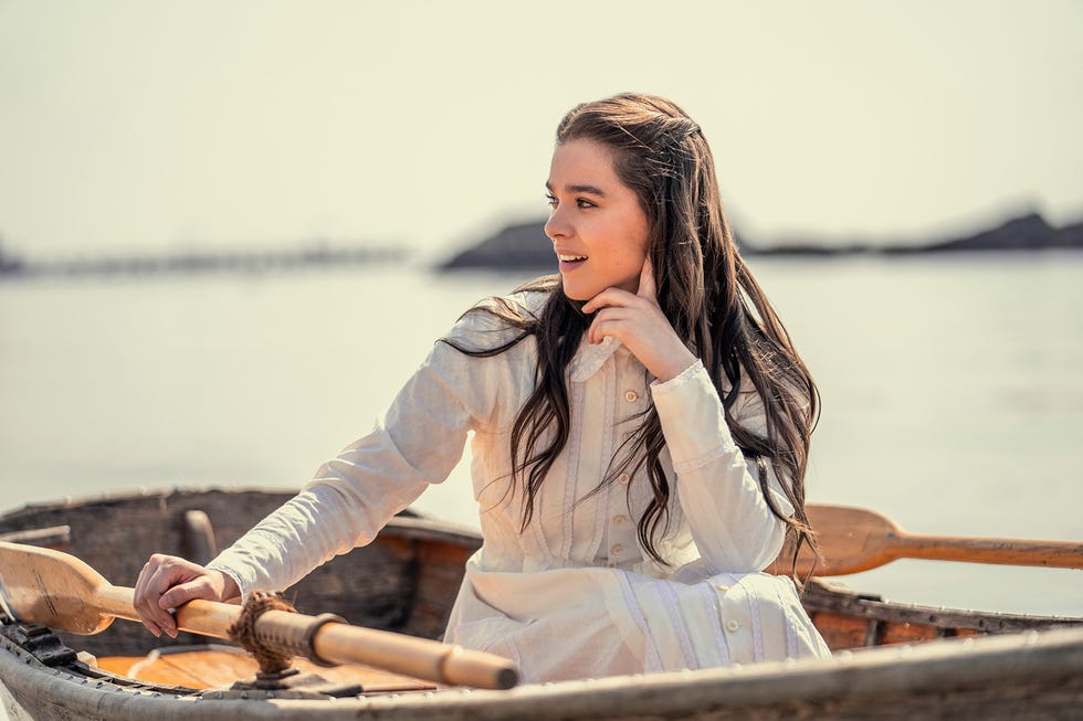 a woman in a white dress sits on a boat and stares to the left over her shoulder