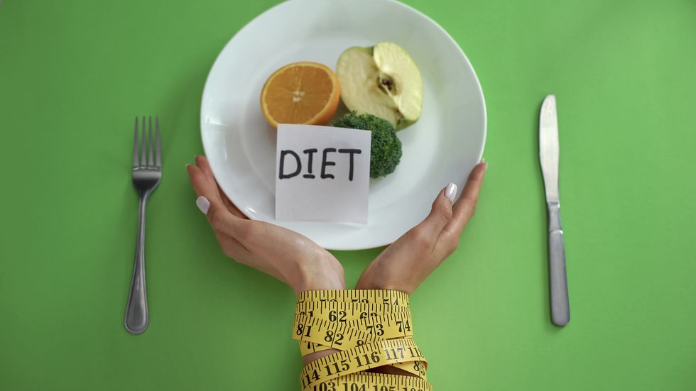 Diet note on plate with fruits and vegetables, hands tied with measuring tape