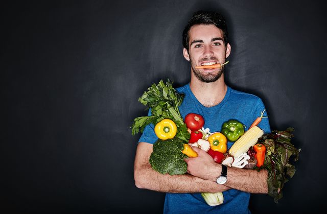 studio portrait of a young man carrying an armful of healthy vegetables against a dark background